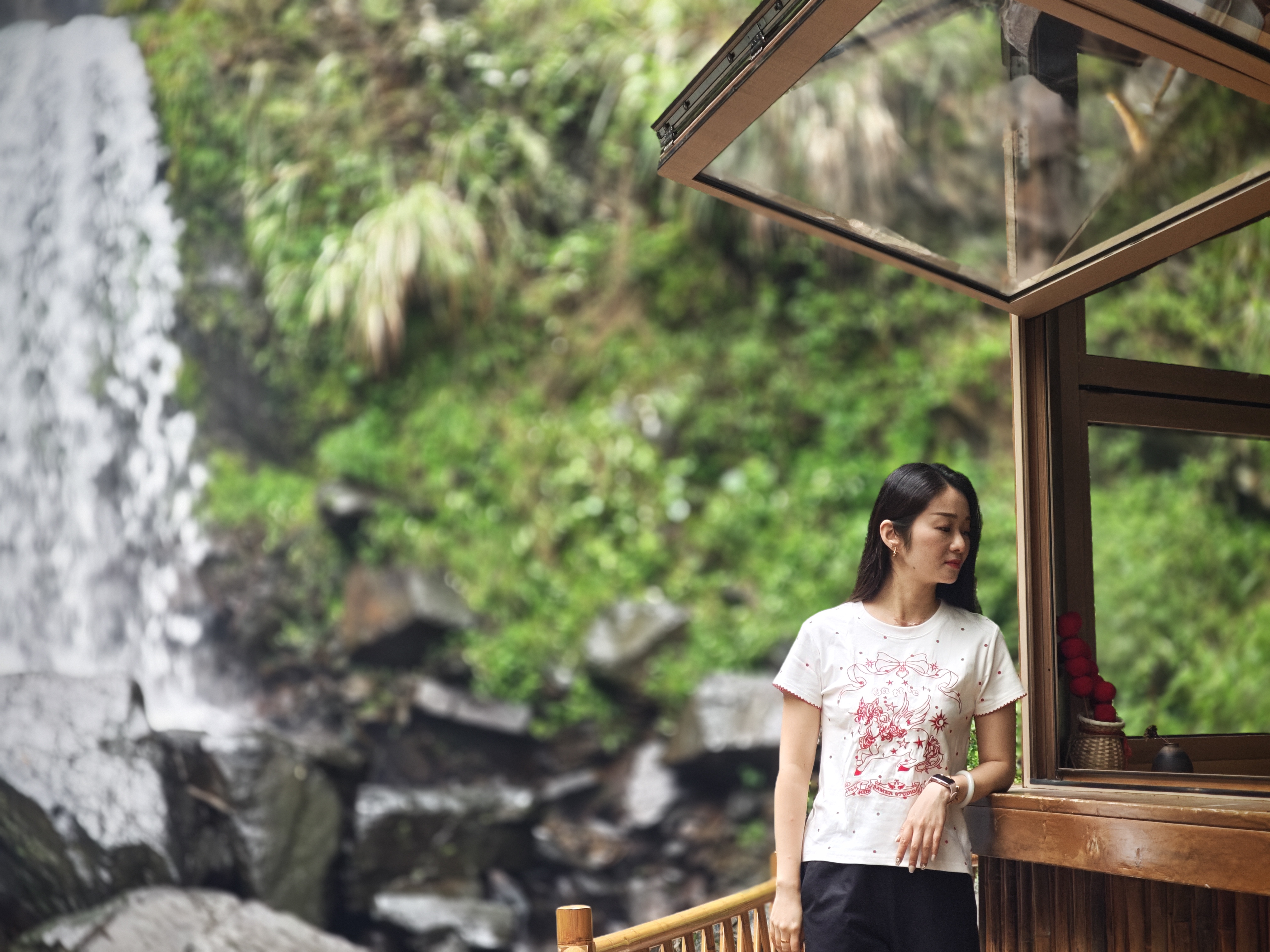 Traveler beside a wooden pavilion and waterfall in a green canyon